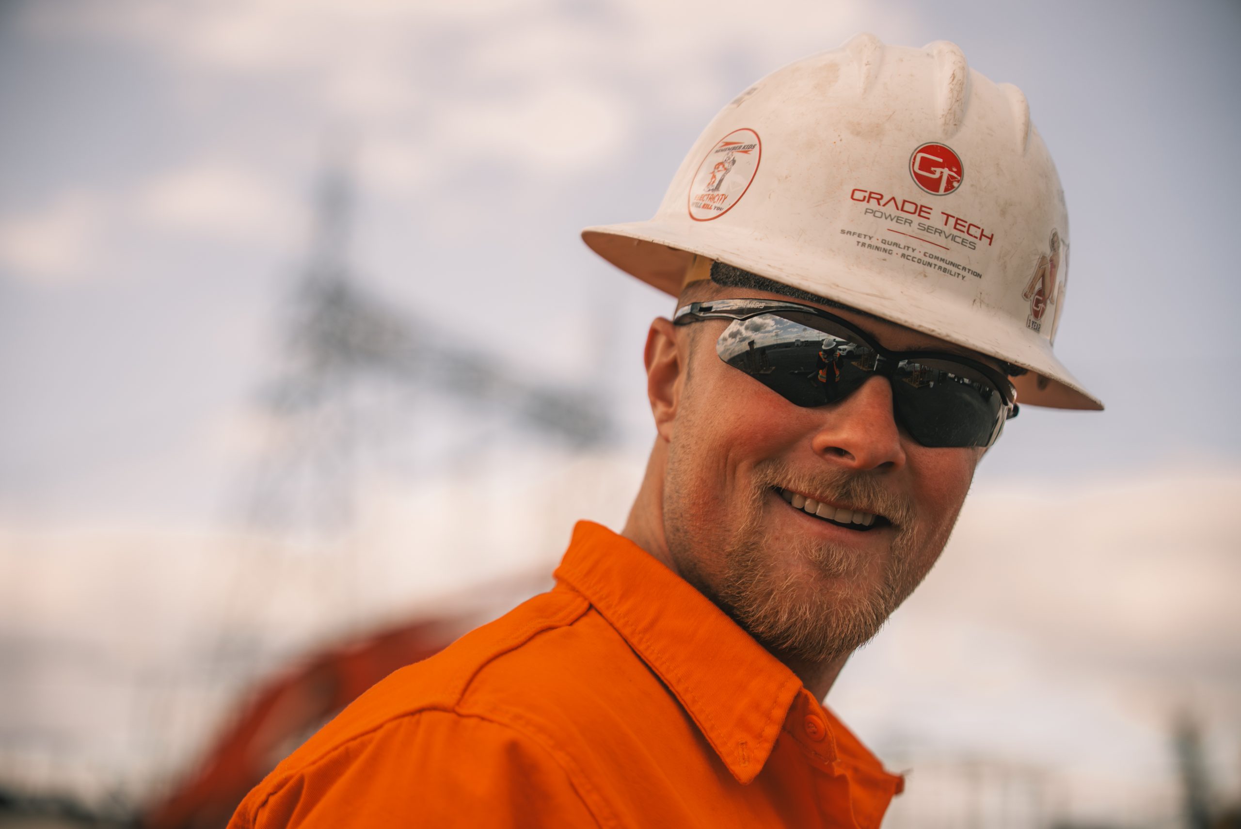 careers-grade-tech-crew-member Smiling Grade Tech crew member in a company hard hat on a substation job